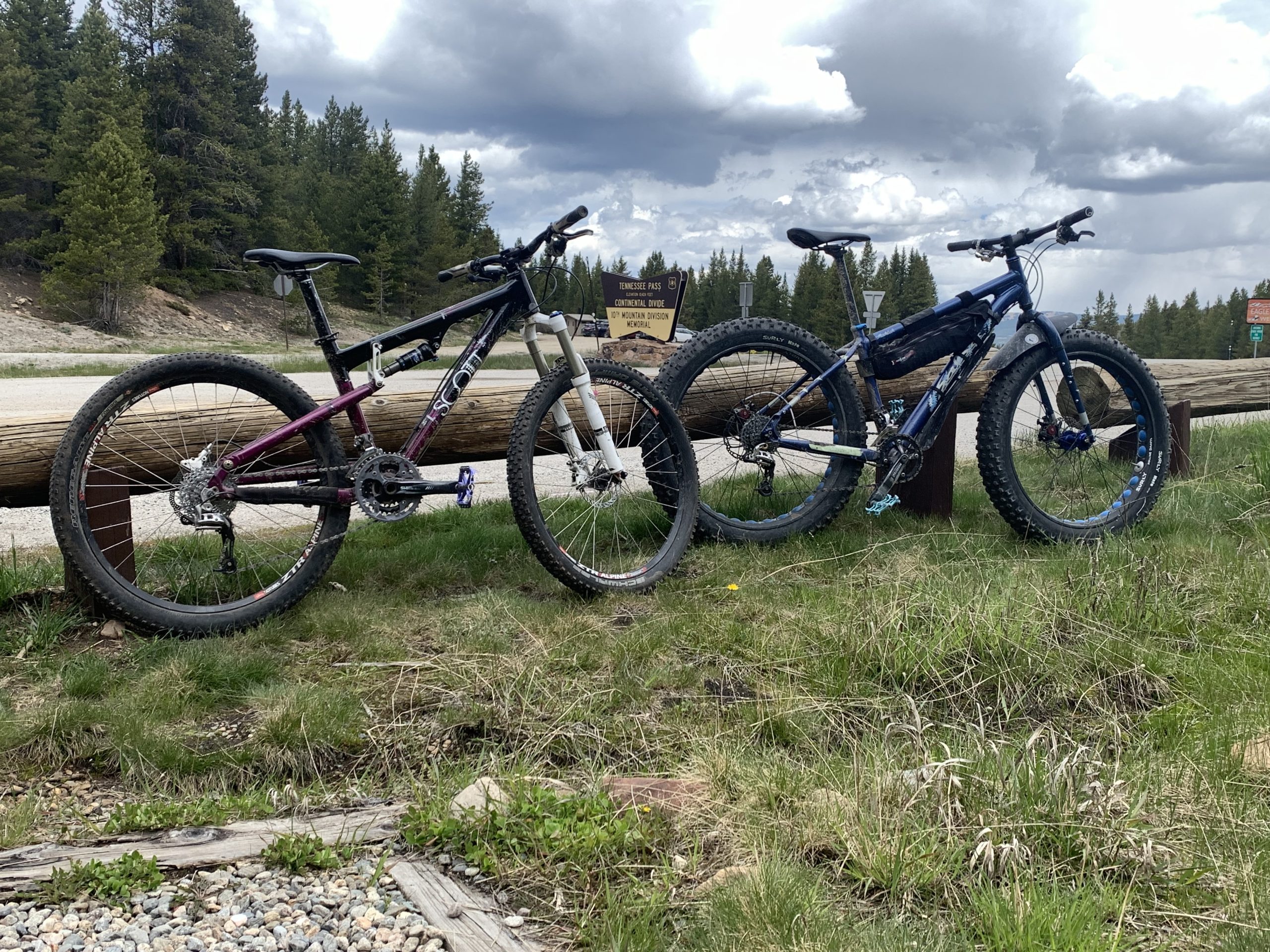 Two mountain bikes leaning against a railing up on a mountain pass.